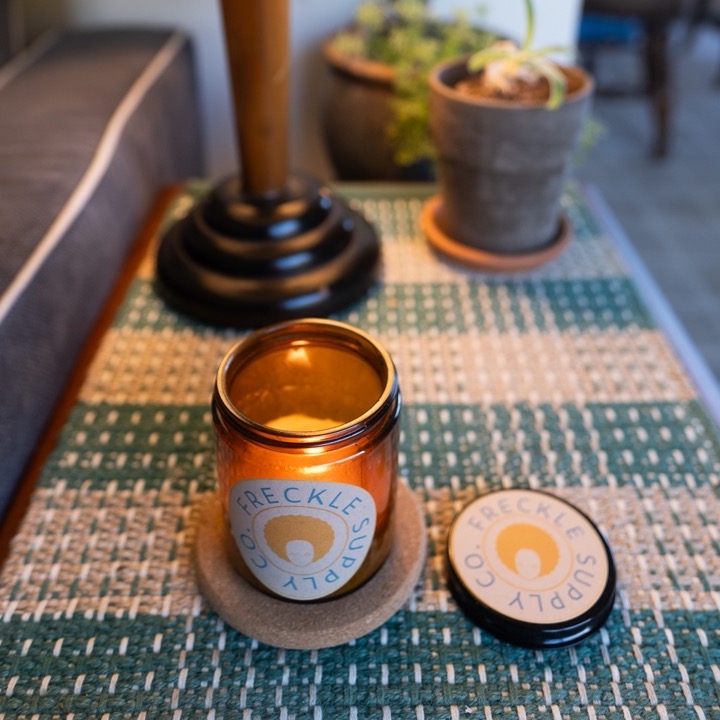 A scented Freckle Supply Co candle on a side table. 